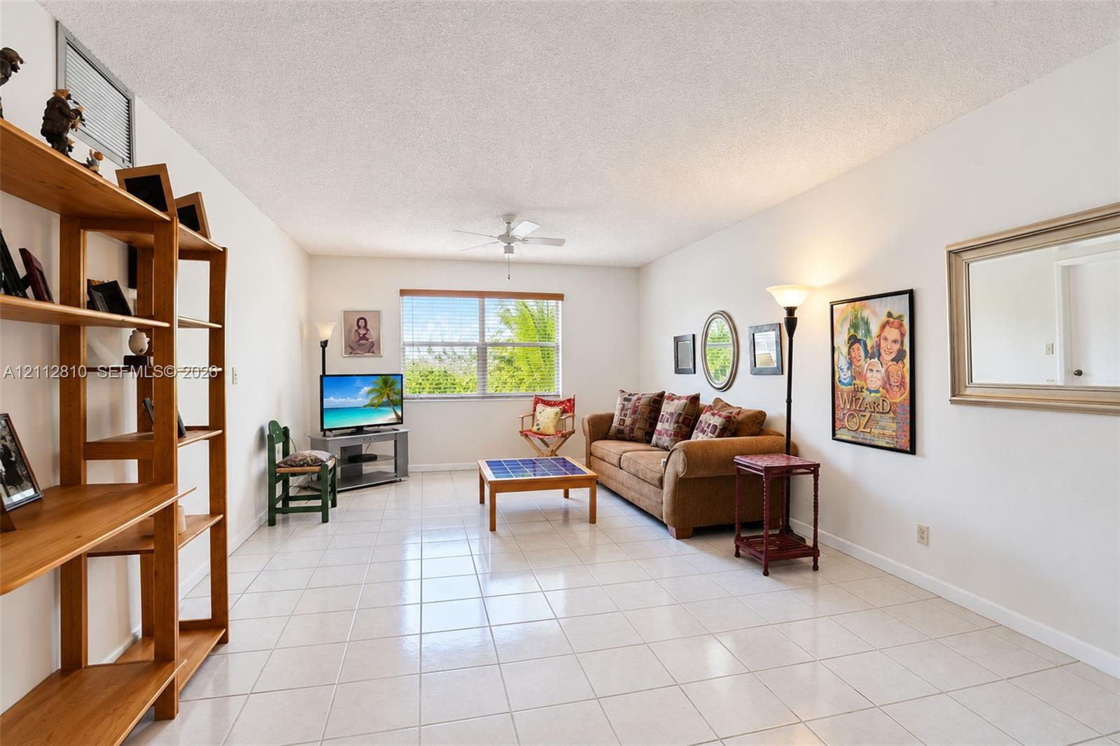 Living area featuring neutral tile flooring, a large picture window, and a ceiling fan with integrated lighting
