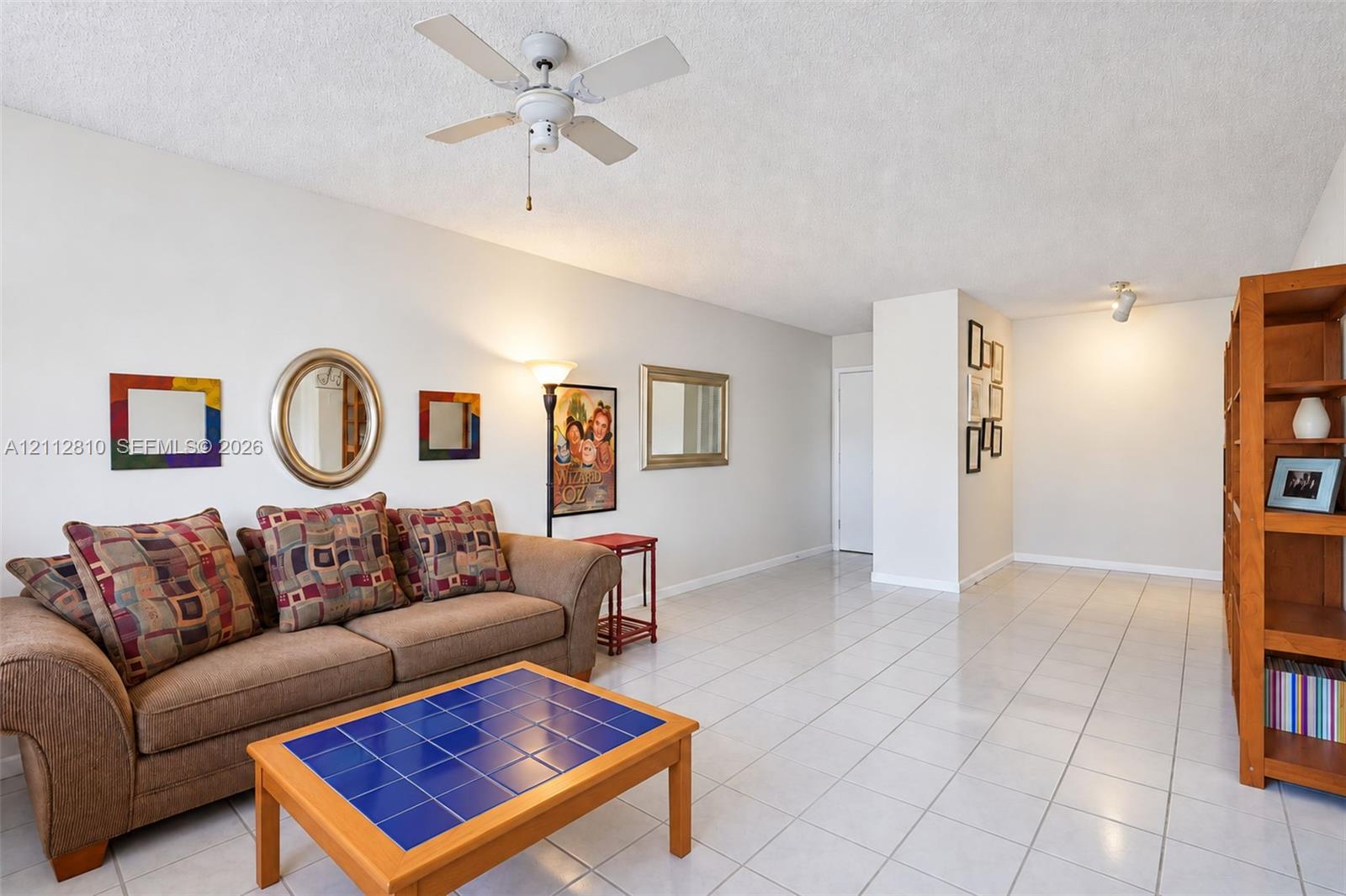 Living area featuring light-toned ceramic tile flooring, a textured ceiling finish, and a center-mounted ceiling fan with light fixture Living area featuring light-toned ceramic tile flooring, a textured ceiling finish, and a center-mounted ceiling fan with light fixture