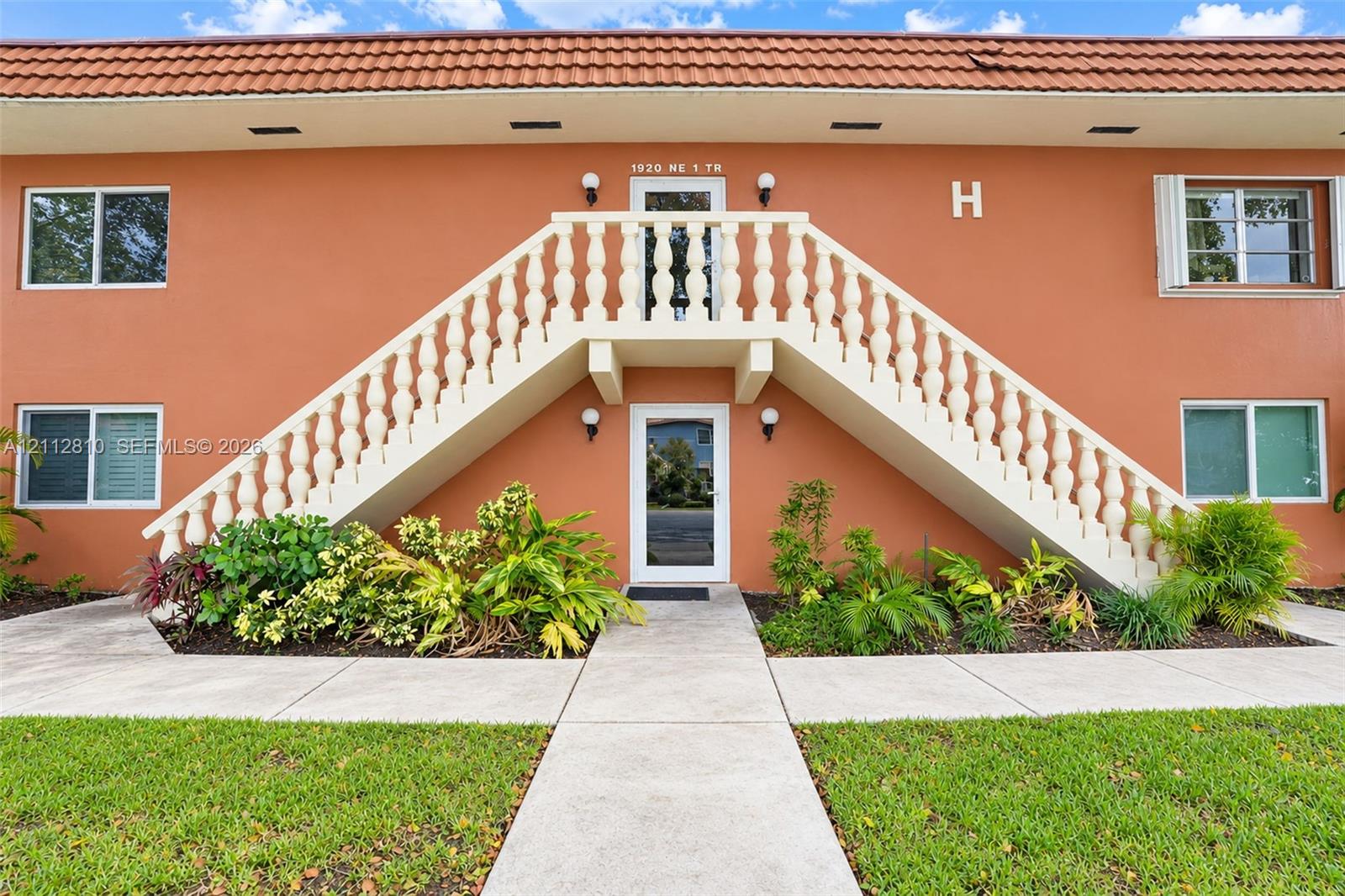 Exterior featuring a stucco facade, clay tile roofing, decorative balustrade staircase, and manicured landscaping