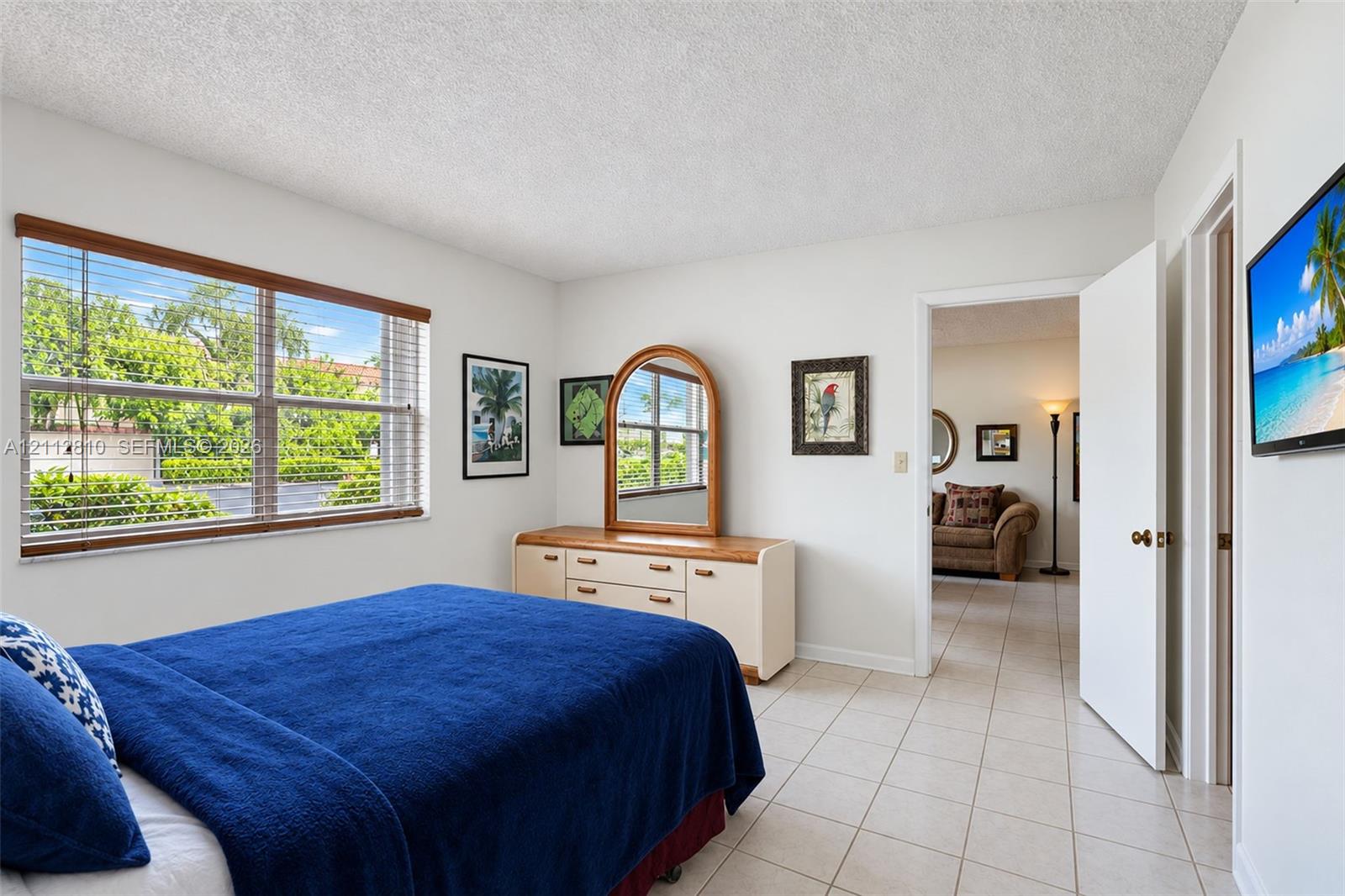 Large horizontal window with wood-finish blinds, neutral ceramic tile flooring, and textured ceiling finish