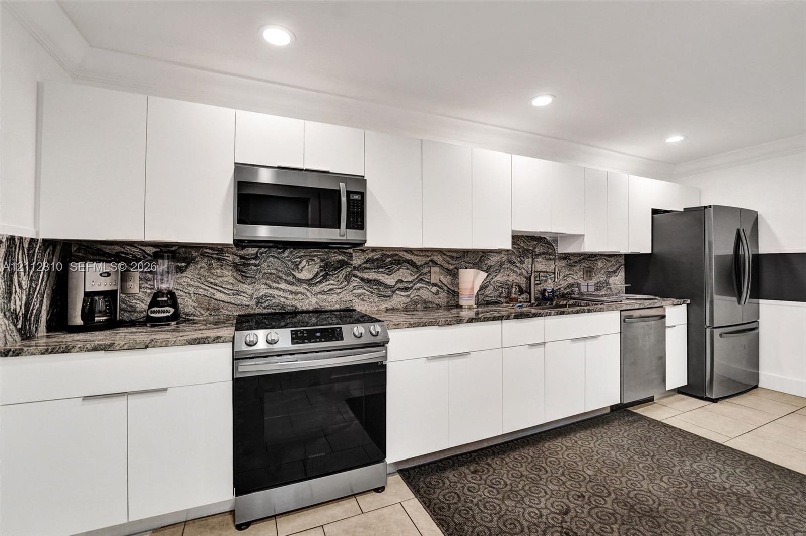 Kitchen featuring flat-panel white cabinetry, stone slab backsplash, stainless steel appliances, and recessed lighting