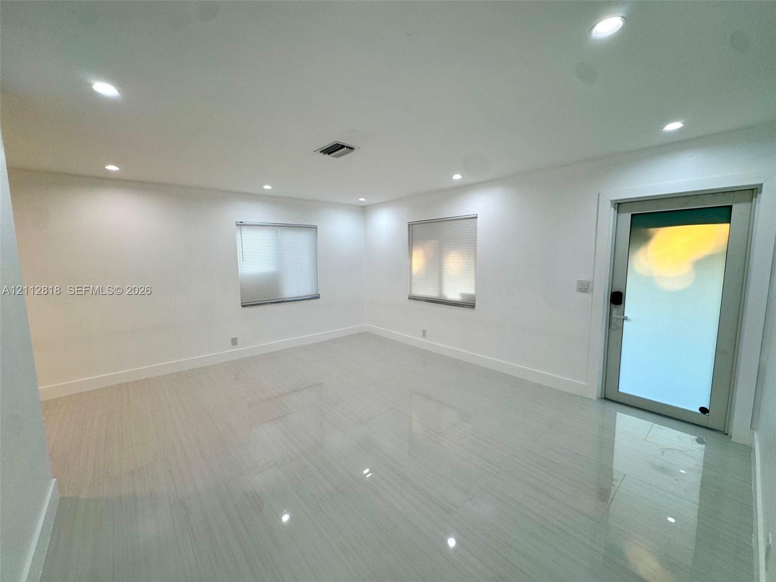 Interior room featuring polished tile flooring, recessed lighting, two windows with blinds, and an exterior door with frosted glass Interior room featuring polished tile flooring, recessed lighting, two windows with blinds, and an exterior door with frosted glass