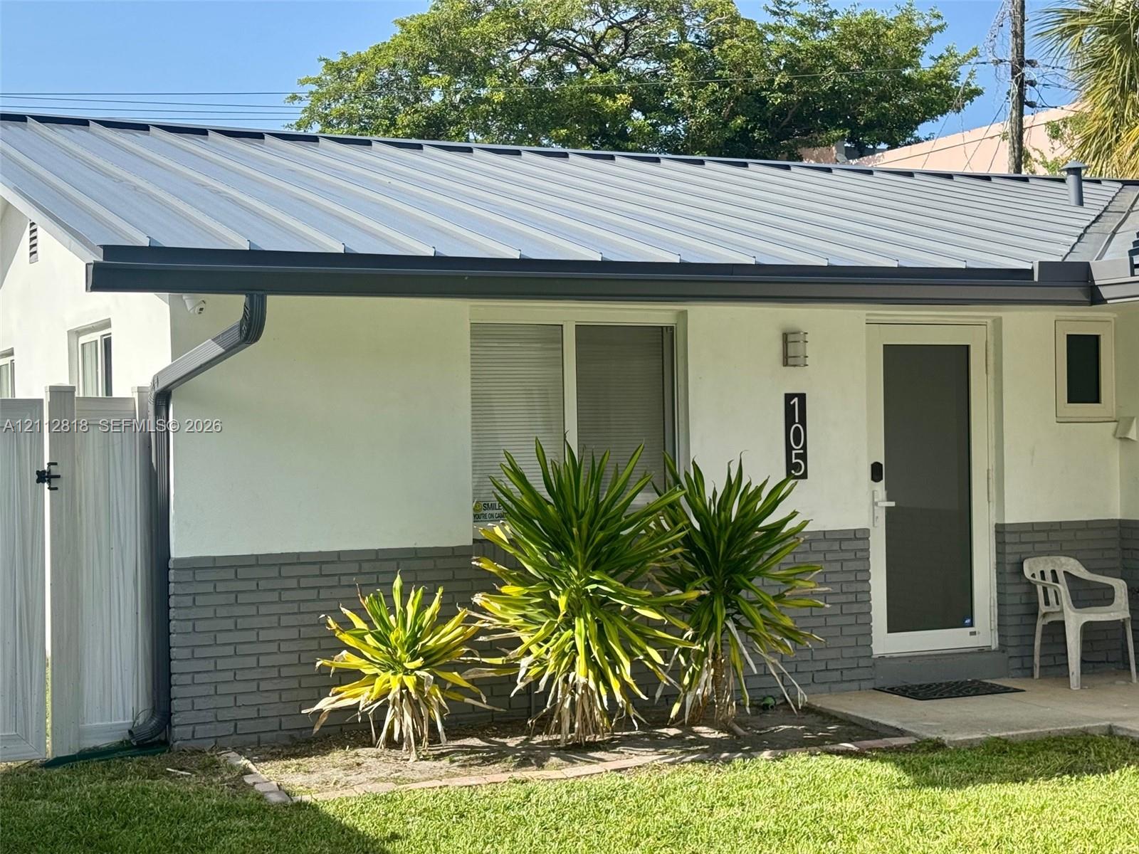 Exterior featuring a standing-seam metal roof, white stucco finish, and gray brick wainscoting with white vinyl fencing