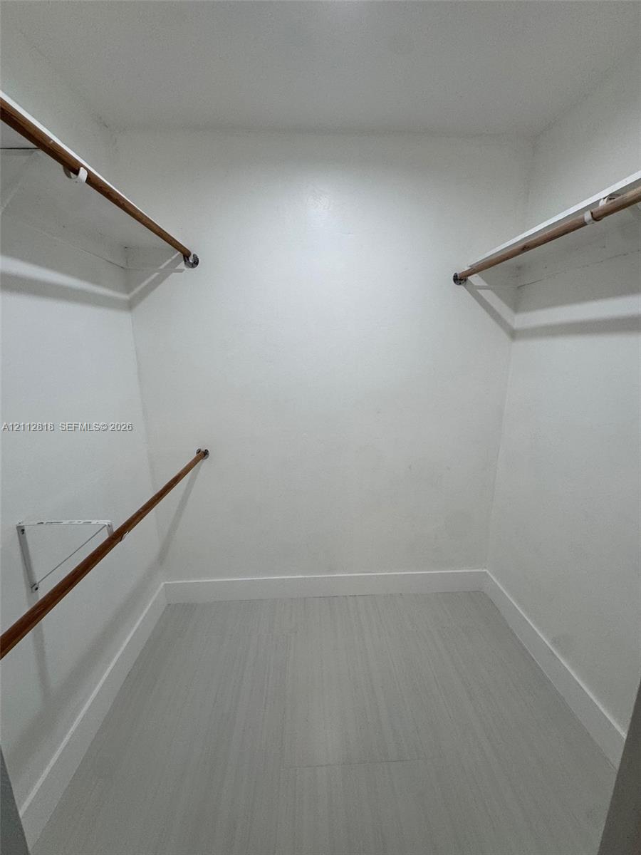 Walk-in storage space featuring wood-finish flooring and tiered metal shelving units with integrated garment rods