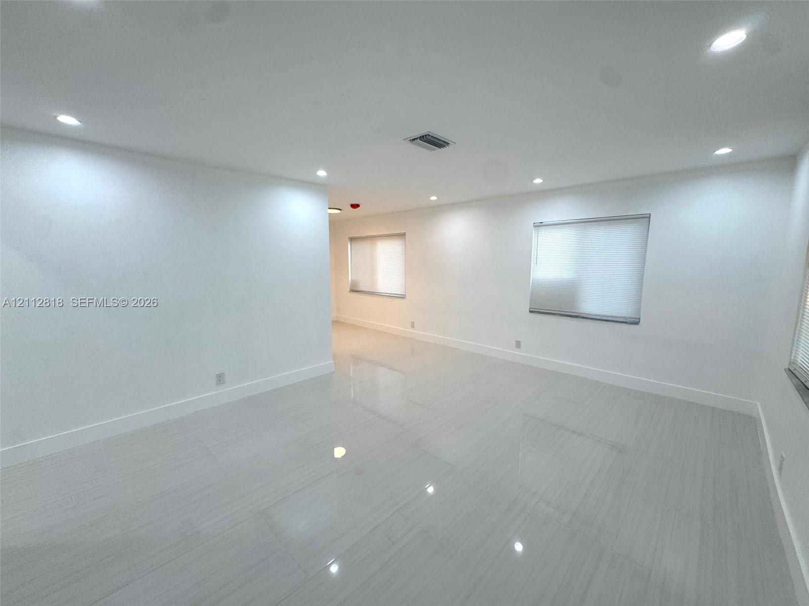 Interior room featuring polished tile flooring, neutral white walls, recessed ceiling lighting, and windows equipped with roller shades Interior room featuring polished tile flooring, neutral white walls, recessed ceiling lighting, and windows equipped with roller shades