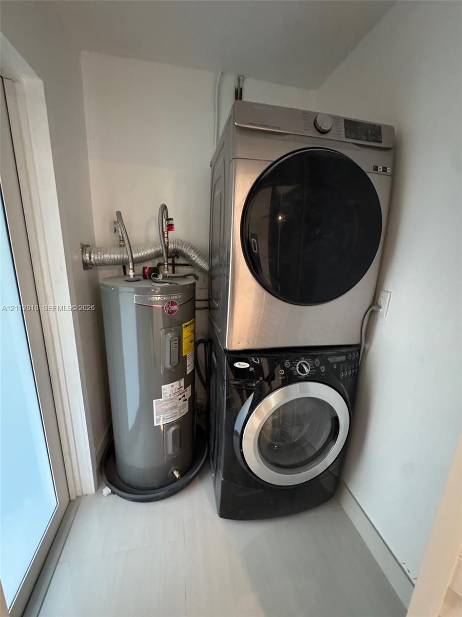 Stacked washer and dryer unit with metallic finish, paired with a cylindrical water heater contained within a dedicated service area