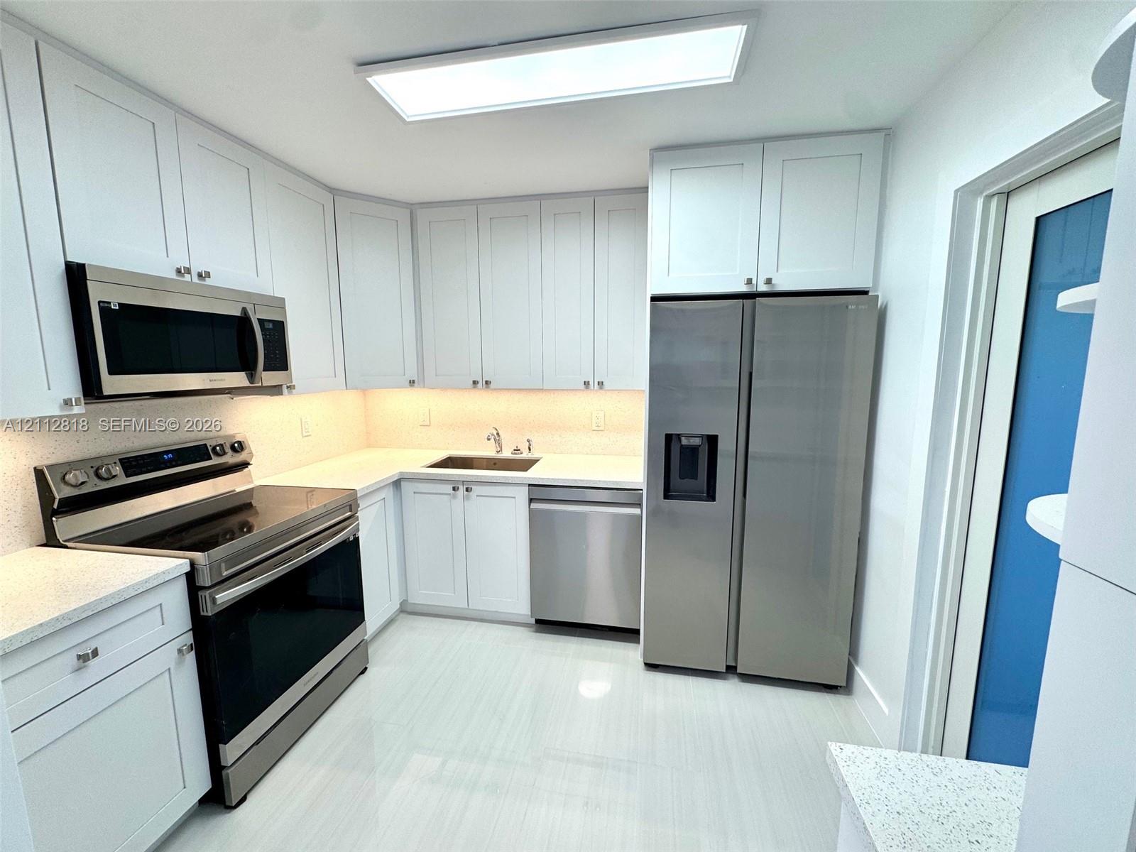 Kitchen featuring white shaker-style cabinetry, stainless steel appliances, solid surface countertops, and light-toned tile flooring Kitchen featuring white shaker-style cabinetry, stainless steel appliances, solid surface countertops, and light-toned tile flooring