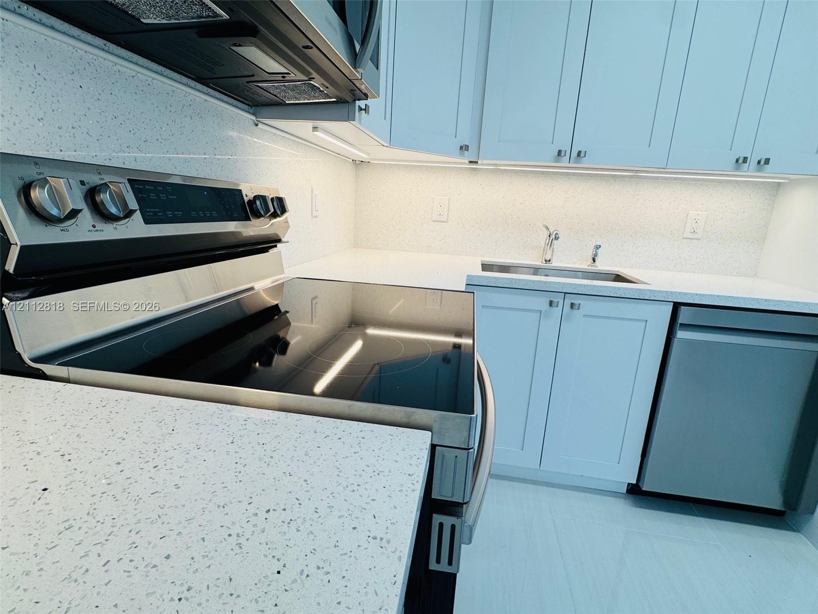 Kitchen featuring shaker-style cabinetry, speckled solid-surface countertops, integrated stainless steel appliances, and under-cabinet lighting Kitchen featuring shaker-style cabinetry, speckled solid-surface countertops, integrated stainless steel appliances, and under-cabinet lighting