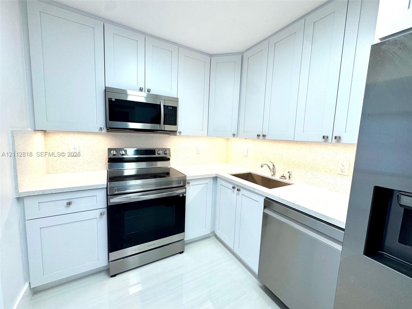Shaker-style cabinetry, stainless steel appliances, light-toned stone-finish countertops, under-cabinet lighting, and integrated sink Shaker-style cabinetry, stainless steel appliances, light-toned stone-finish countertops, under-cabinet lighting, and integrated sink
