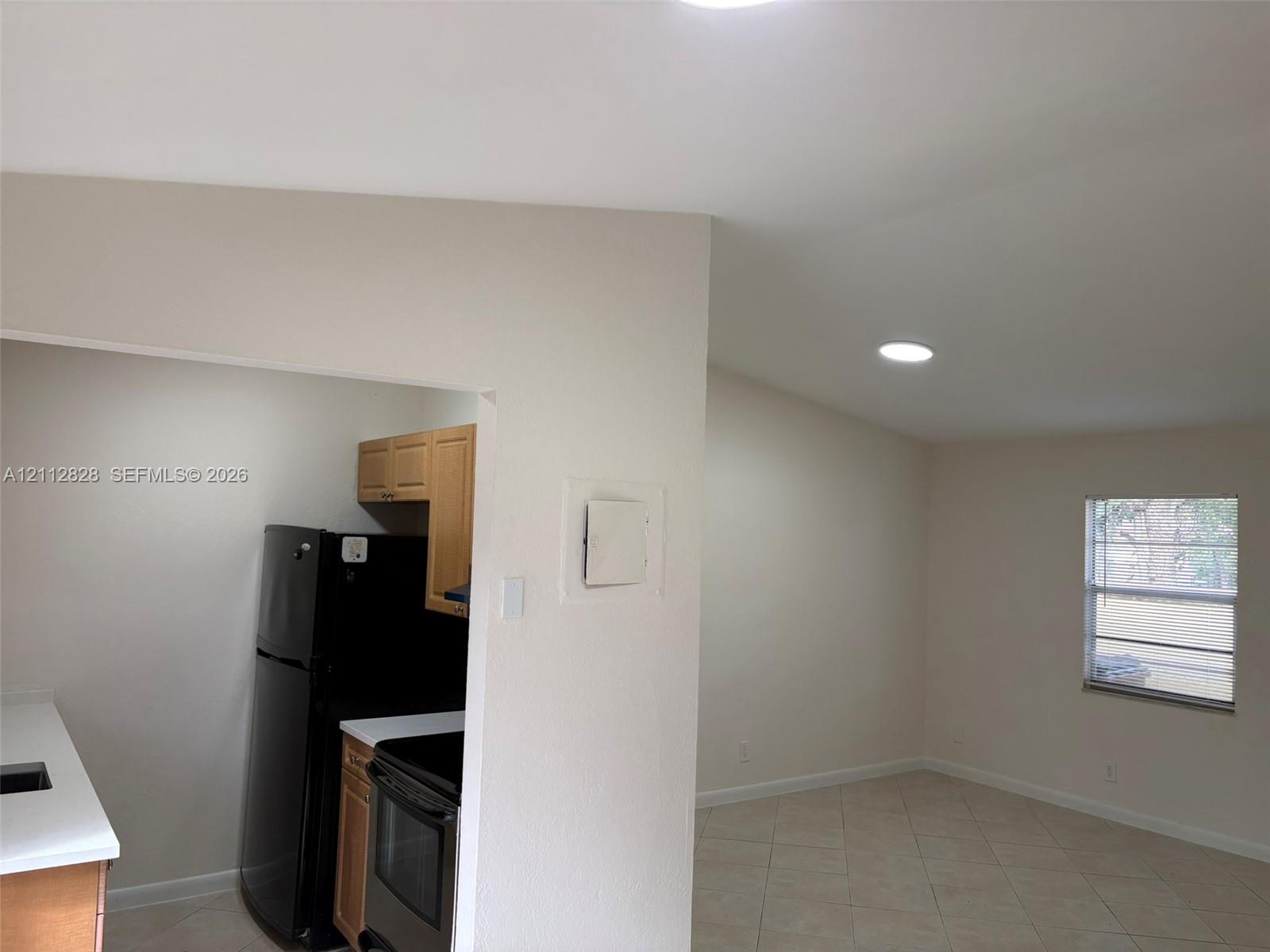 Kitchen area featuring light-finish cabinetry, solid-surface countertops, and black appliances, complemented by tile flooring and recessed lighting throughout