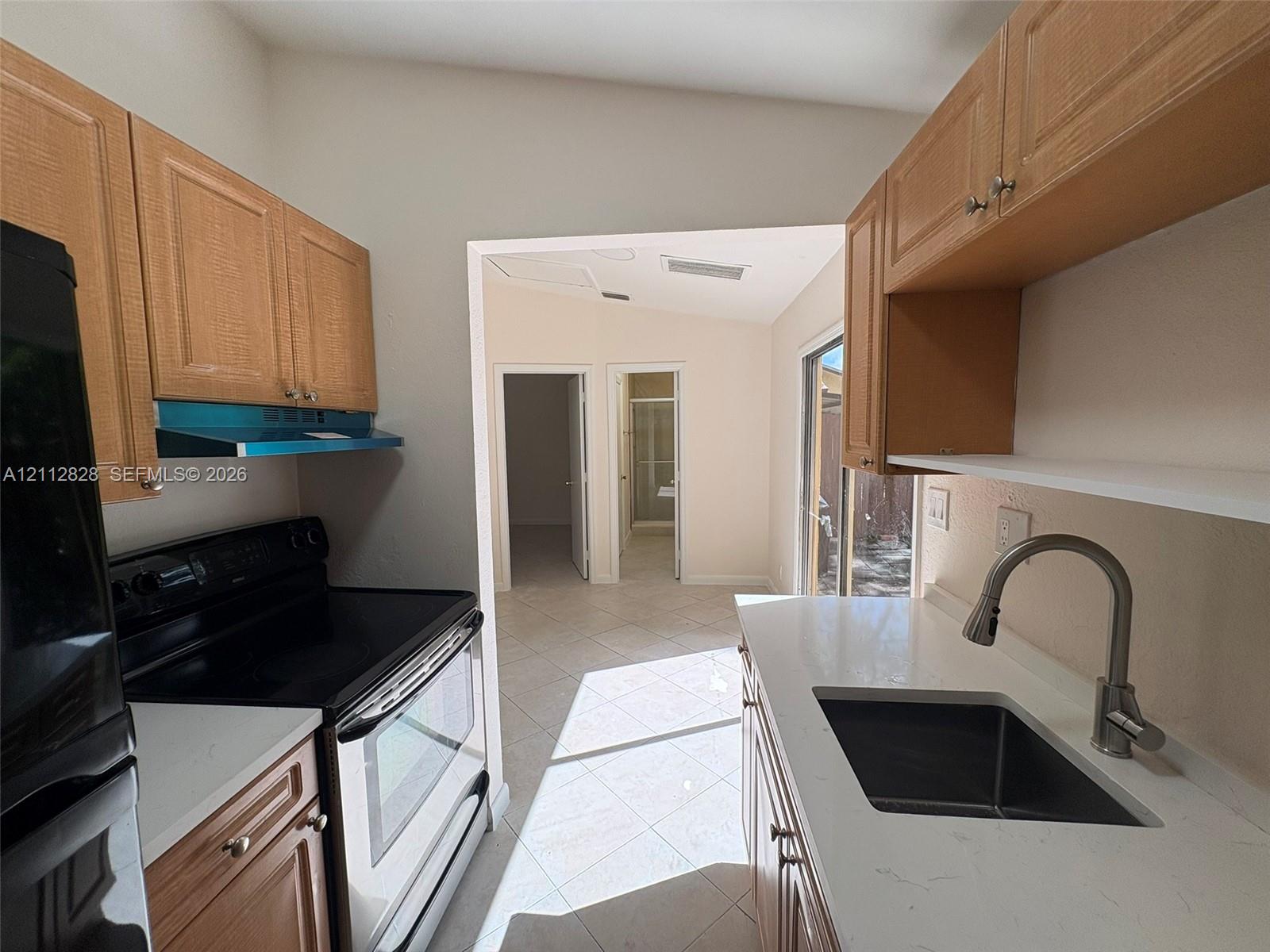 Kitchen featuring wood-finish cabinetry, white solid-surface countertops, a stainless steel undermount sink with a gooseneck faucet, and tile flooring