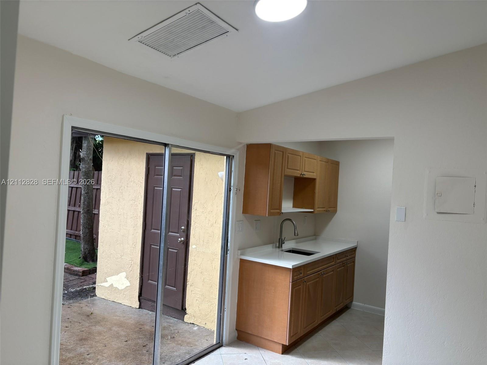 Kitchen featuring wood cabinetry, white countertops, and a stainless steel sink with a gooseneck faucet, accompanied by sliding glass doors opening to an exterior patio with a textured wall finish