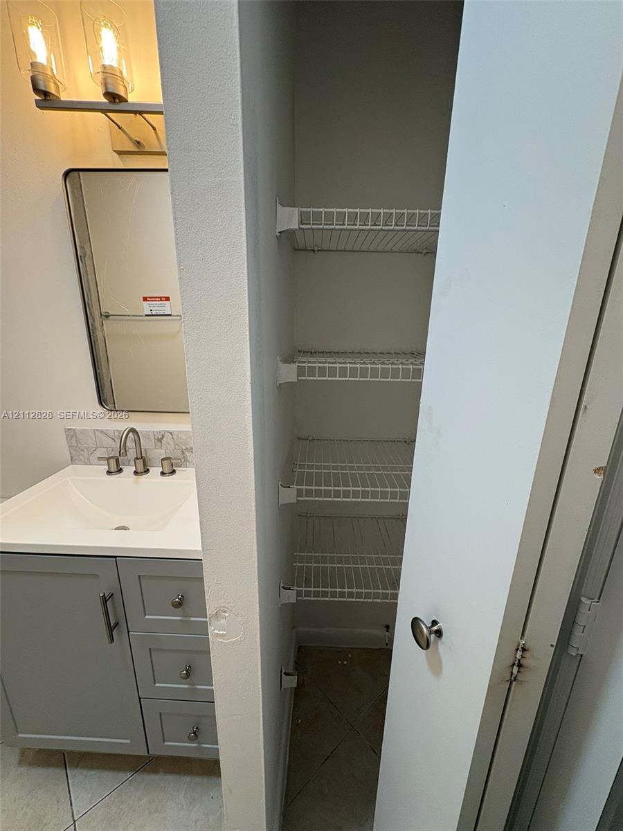 Vanity featuring grey shaker-style cabinetry, a solid-surface countertop with an integrated basin, a polished nickel widespread faucet, and a rectangular mirror