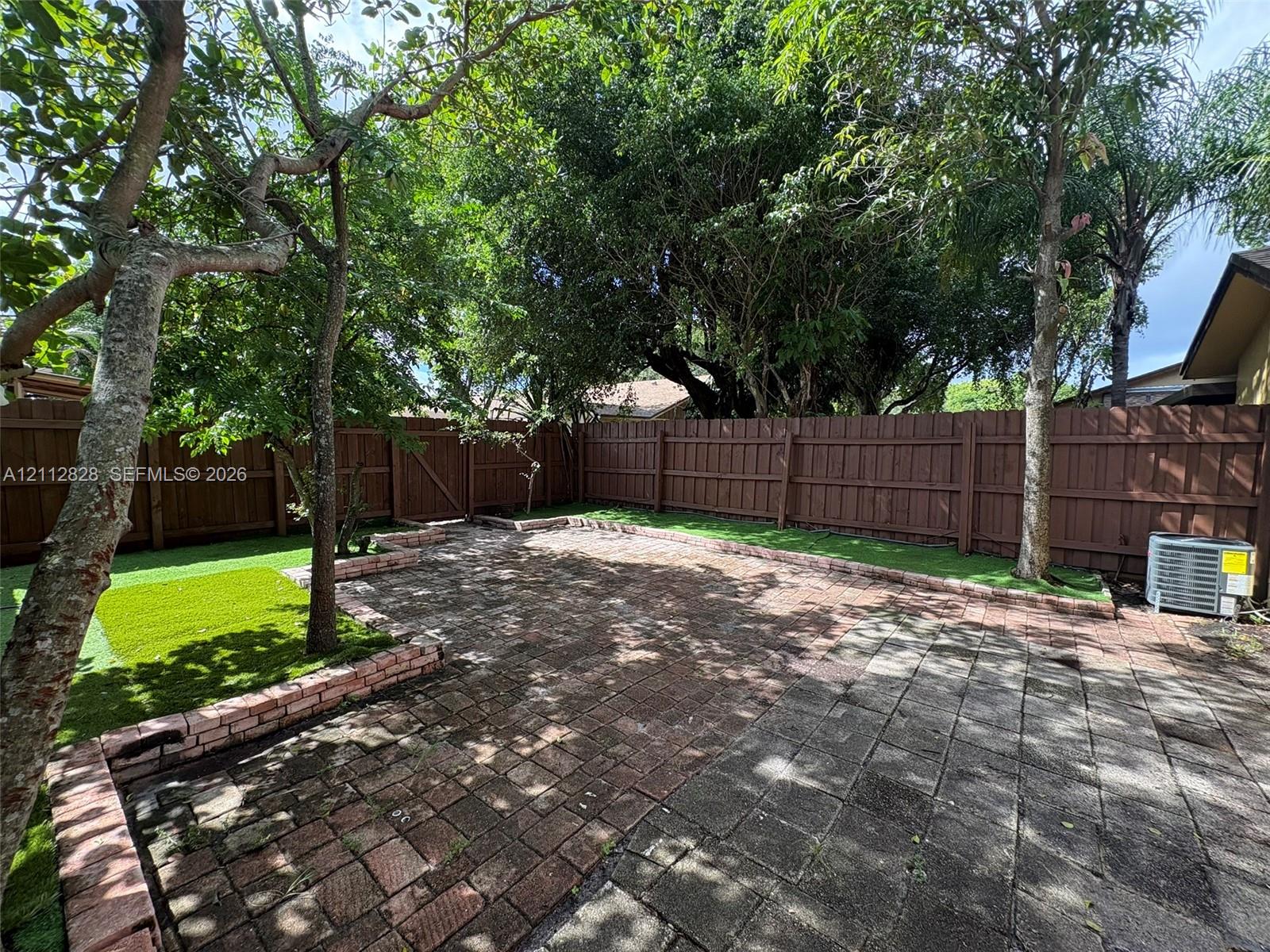 Rear yard featuring a paver patio, brick retaining walls, synthetic turf, wood privacy fencing, and mature trees