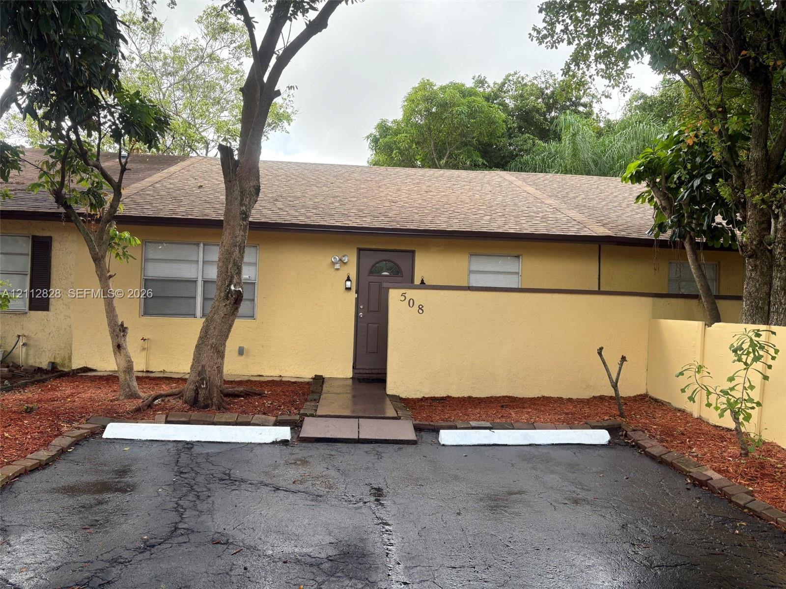Stucco exterior featuring a paved parking area with dual wheel stops, a walkway to the front entry, and masonry privacy wall