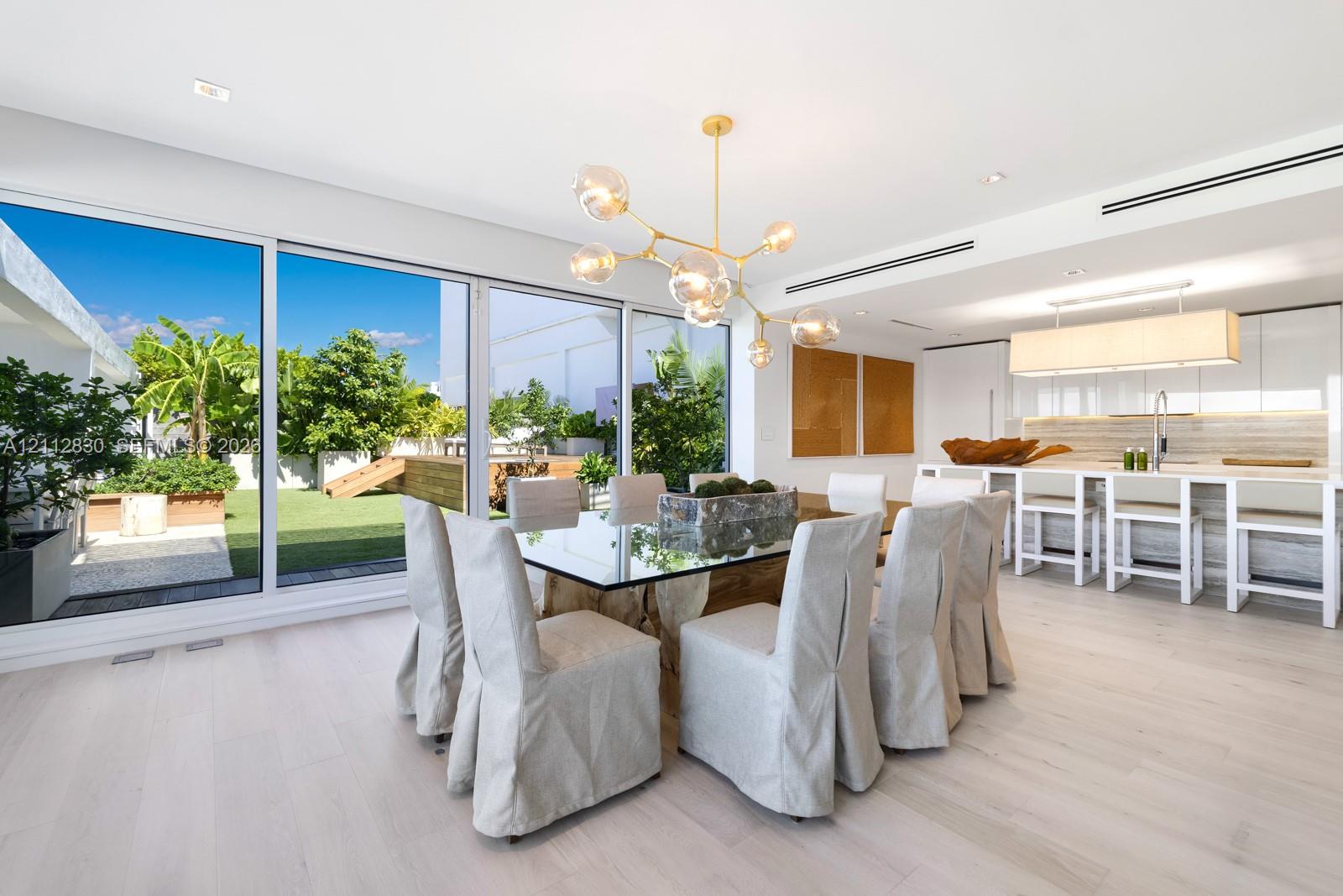 Floor-to-ceiling sliding glass panels, wood-finish flooring, linear recessed lighting, brass-finish multi-arm chandelier, and white flat-panel cabinetry