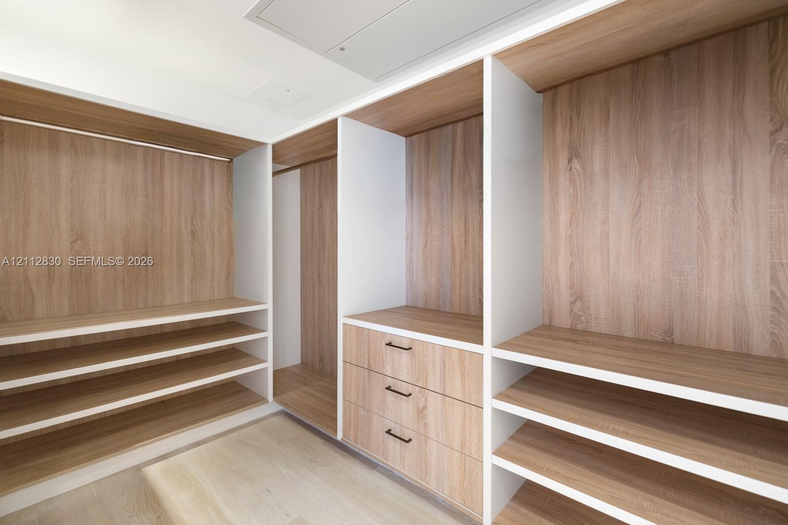 Custom walk-in closet featuring wood-finish cabinetry, built-in shelving, integrated hanging rods, and a three-drawer storage unit with matte black hardware
