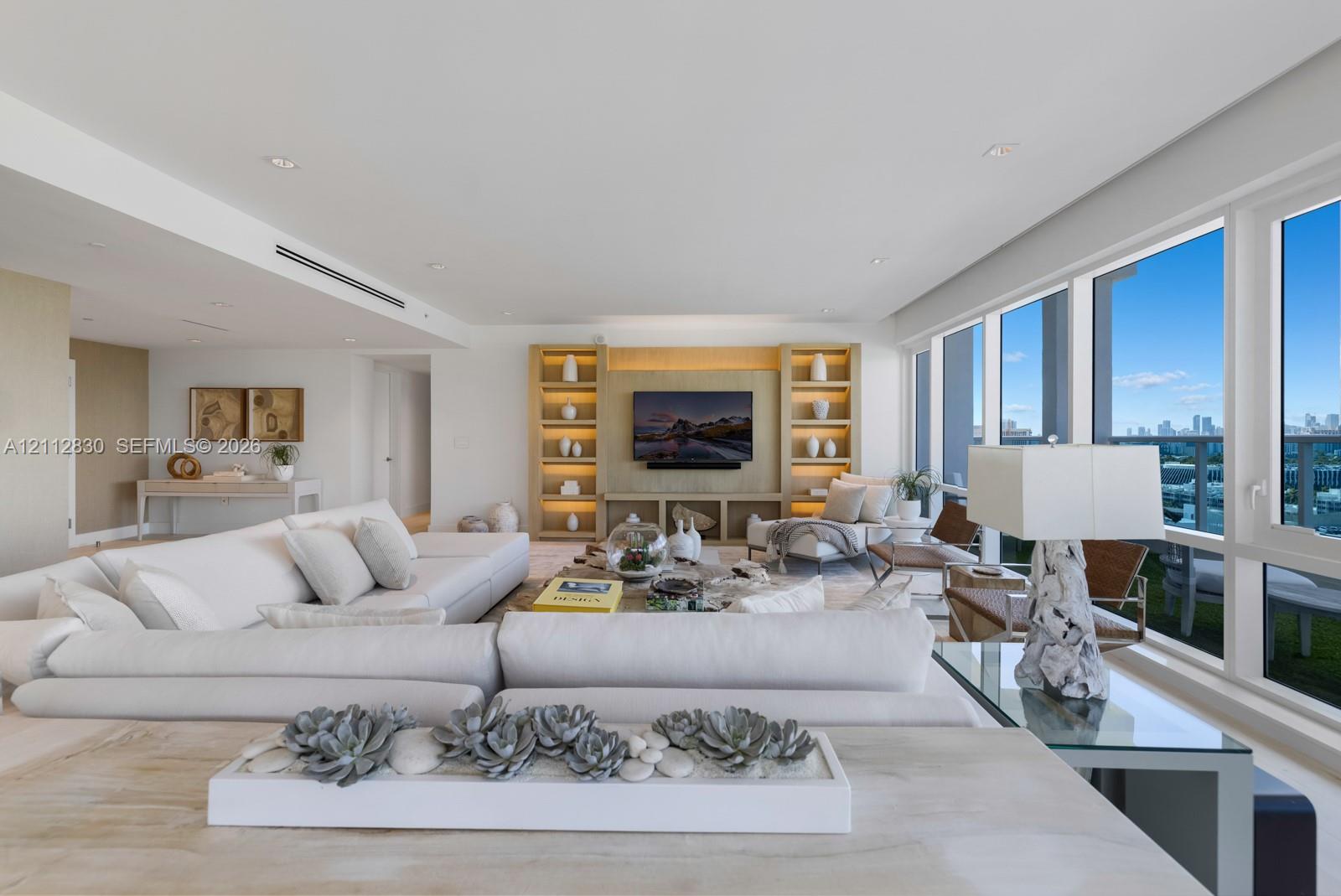 Open-concept interior featuring floor-to-ceiling windows, custom built-in cabinetry with integrated shelving, recessed lighting, and smooth-finish walls