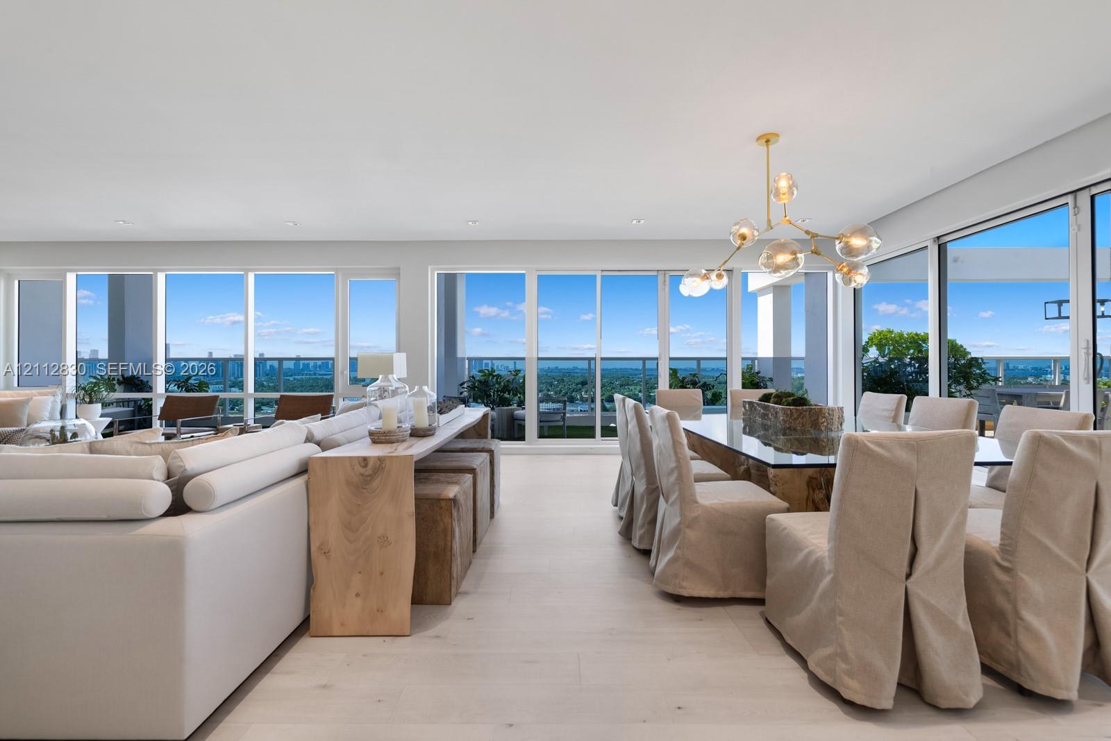 Expansive open floor plan featuring floor-to-ceiling glass walls, wood-finish flooring, recessed lighting, and a multi-globe branching chandelier