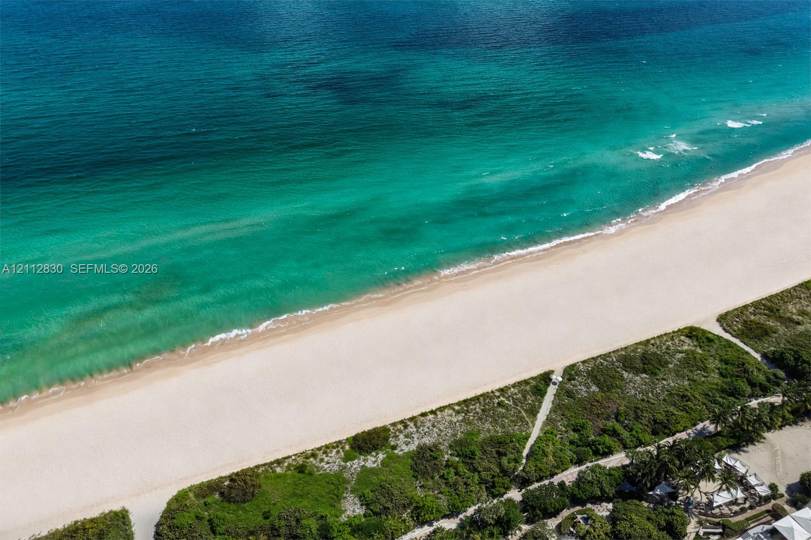 Direct oceanfront access featuring expansive sandy shoreline, turquoise water, and native coastal vegetation