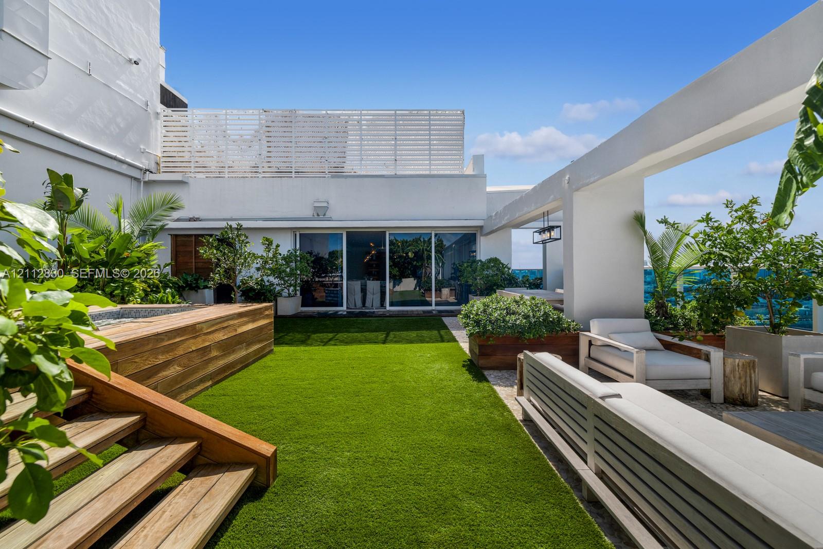 Rooftop terrace featuring artificial turf, tiered wood-finish stairs, a recessed spa, a pergola structure, and built-in wood-finish planters