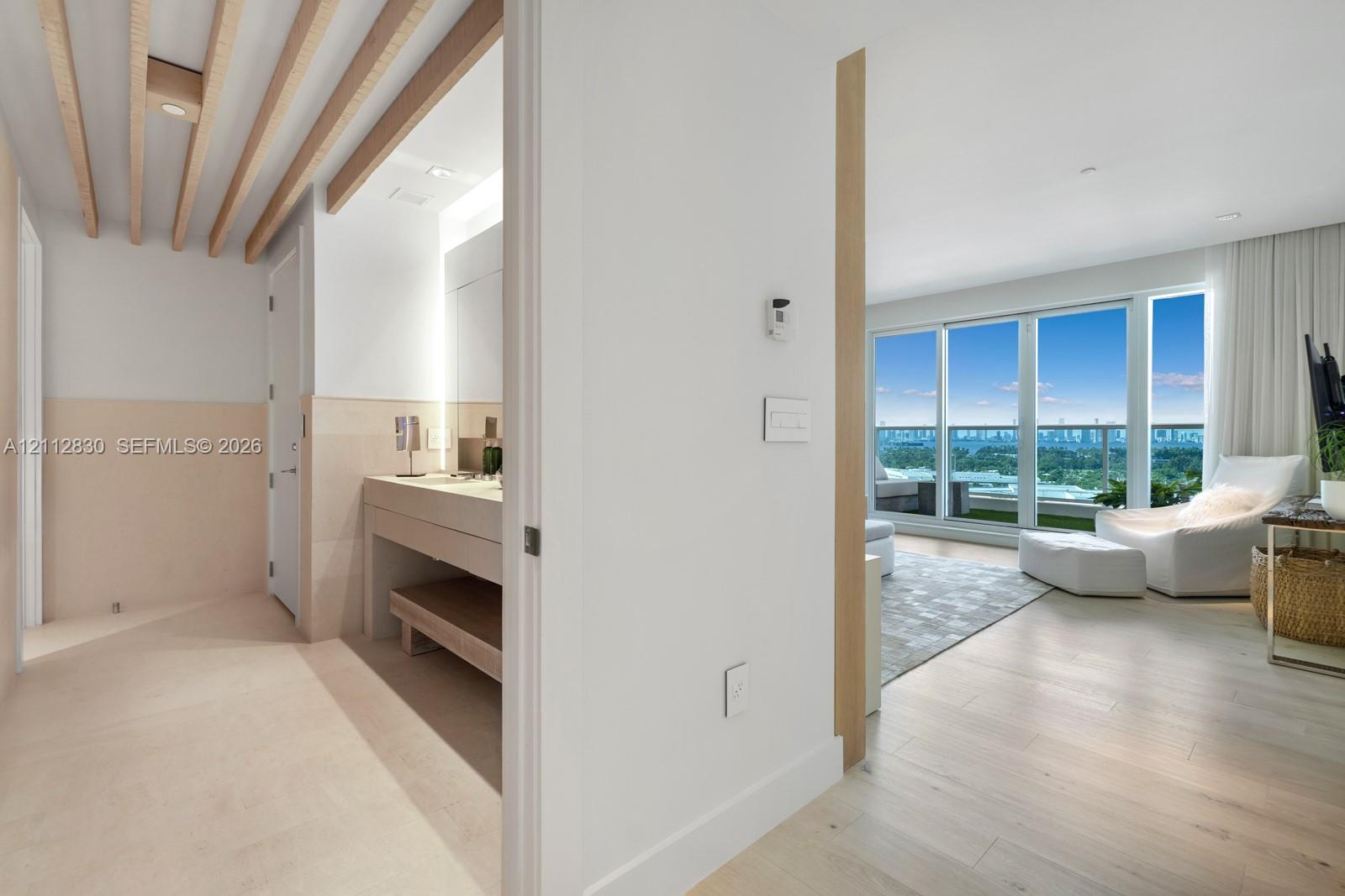 Light-filled interior featuring floor-to-ceiling windows, wood-finish flooring, exposed ceiling beams, a built-in vanity with under-counter shelving, and a balcony with a glass railing