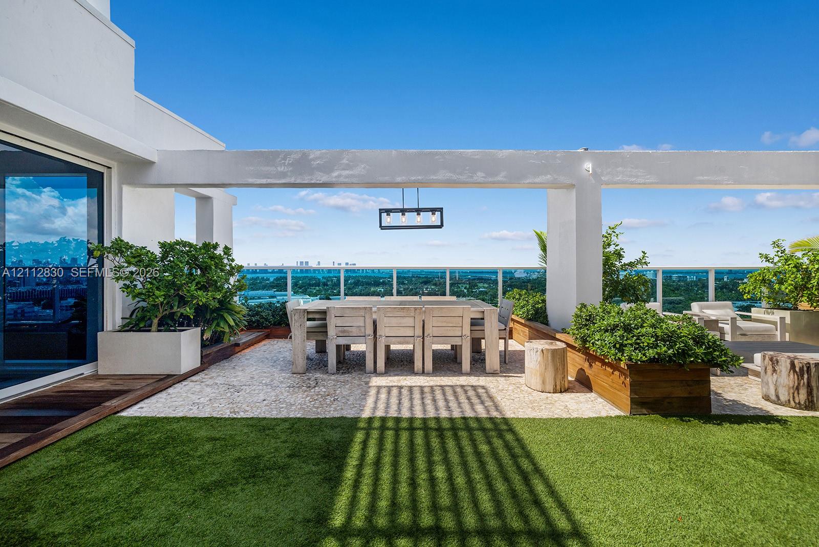 Rooftop terrace featuring synthetic turf, stone-paver flooring, a built-in pergola, integrated planter boxes, and a linear pendant light fixture