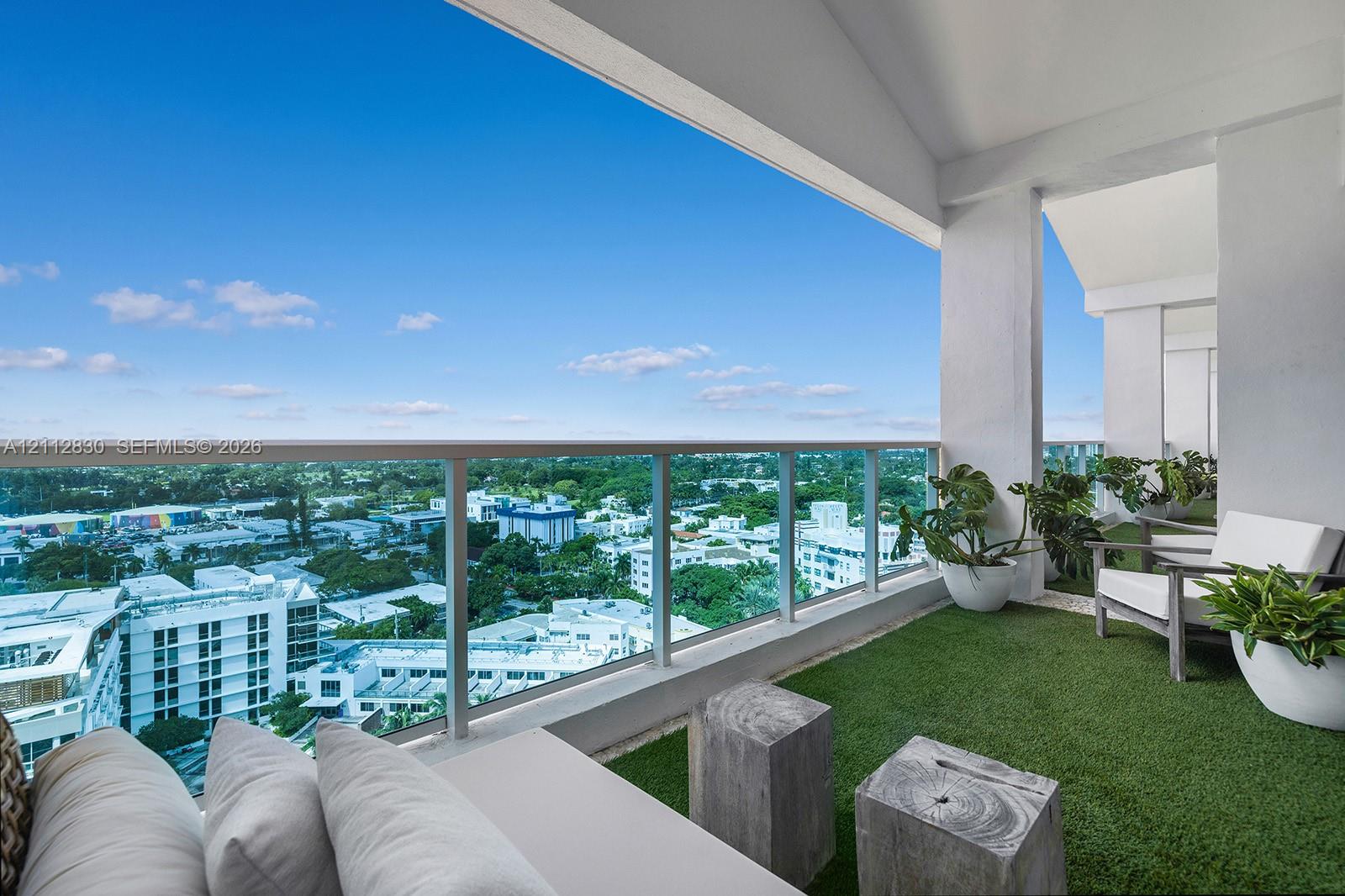 Covered balcony featuring a glass panel railing, artificial turf flooring, and expansive urban scenery