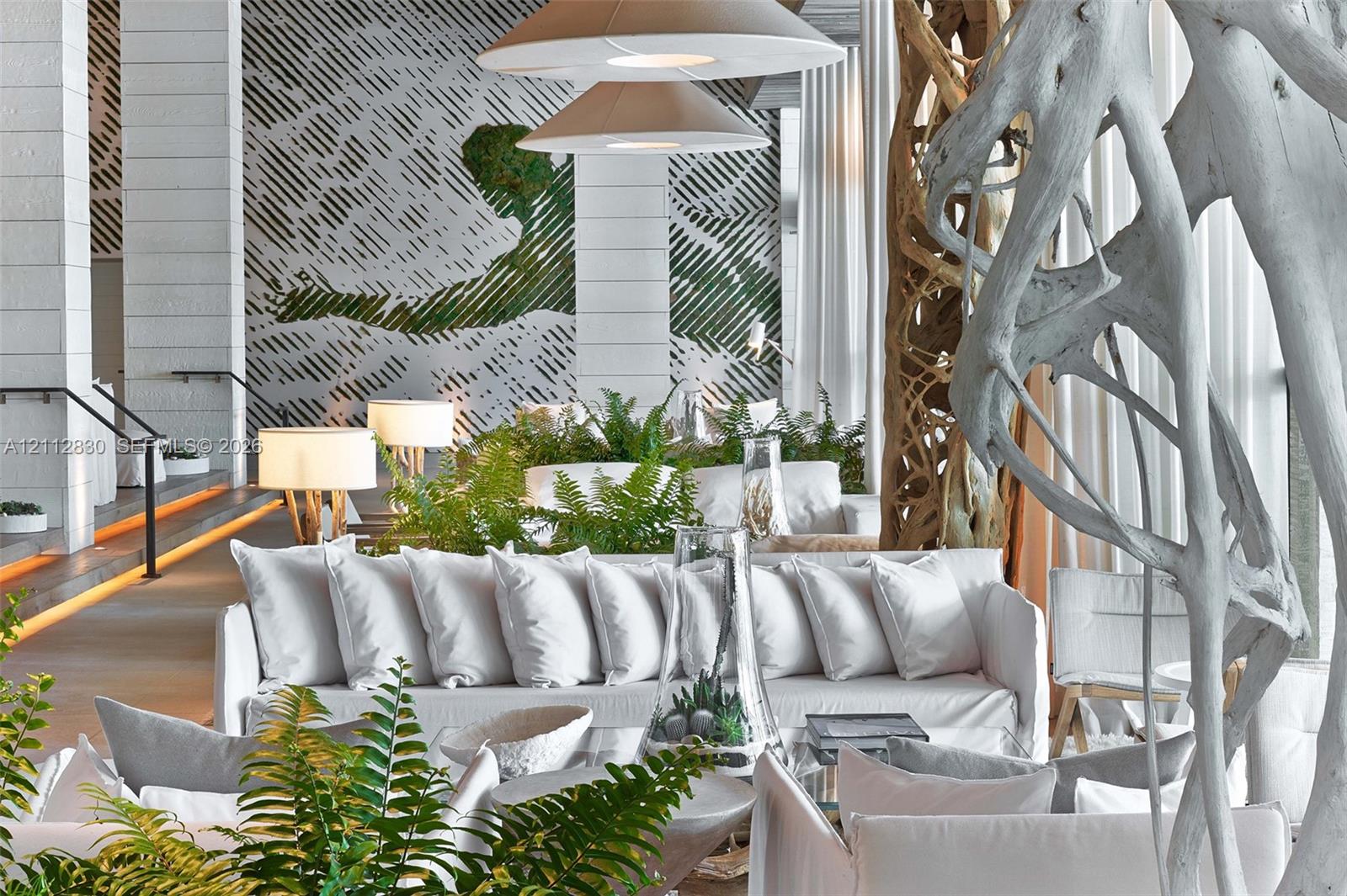 Expansive interior featuring large-format stone wall cladding, custom sculpted organic wood pillar, recessed floor accent lighting, and dual conical pendant fixtures