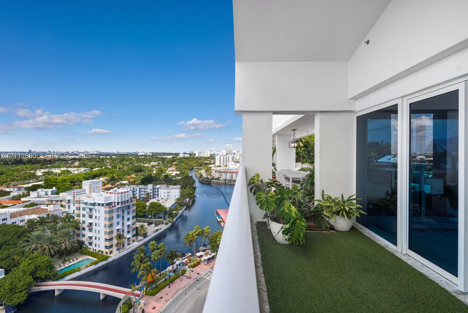 Covered outdoor balcony featuring synthetic turf surfacing, a solid white structural railing, and multi-panel floor-to-ceiling glass sliding doors