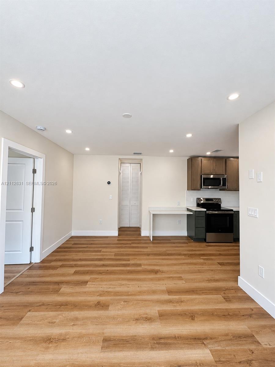 Open-concept interior featuring wood-finish flooring, recessed lighting, white cabinetry, integrated stainless steel appliances, and a built-in counter surface Open-concept interior featuring wood-finish flooring, recessed lighting, white cabinetry, integrated stainless steel appliances, and a built-in counter surface