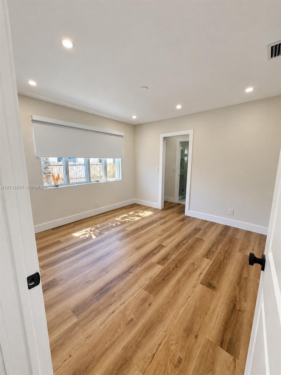 Room featuring wood-finish flooring, recessed lighting, neutral wall paint, and windows with integrated roller shades