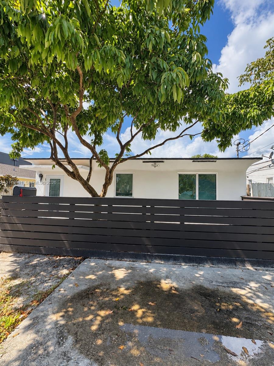 Stucco exterior featuring horizontal slat privacy fencing, dual-pane windows, and a mature shade tree Stucco exterior featuring horizontal slat privacy fencing, dual-pane windows, and a mature shade tree