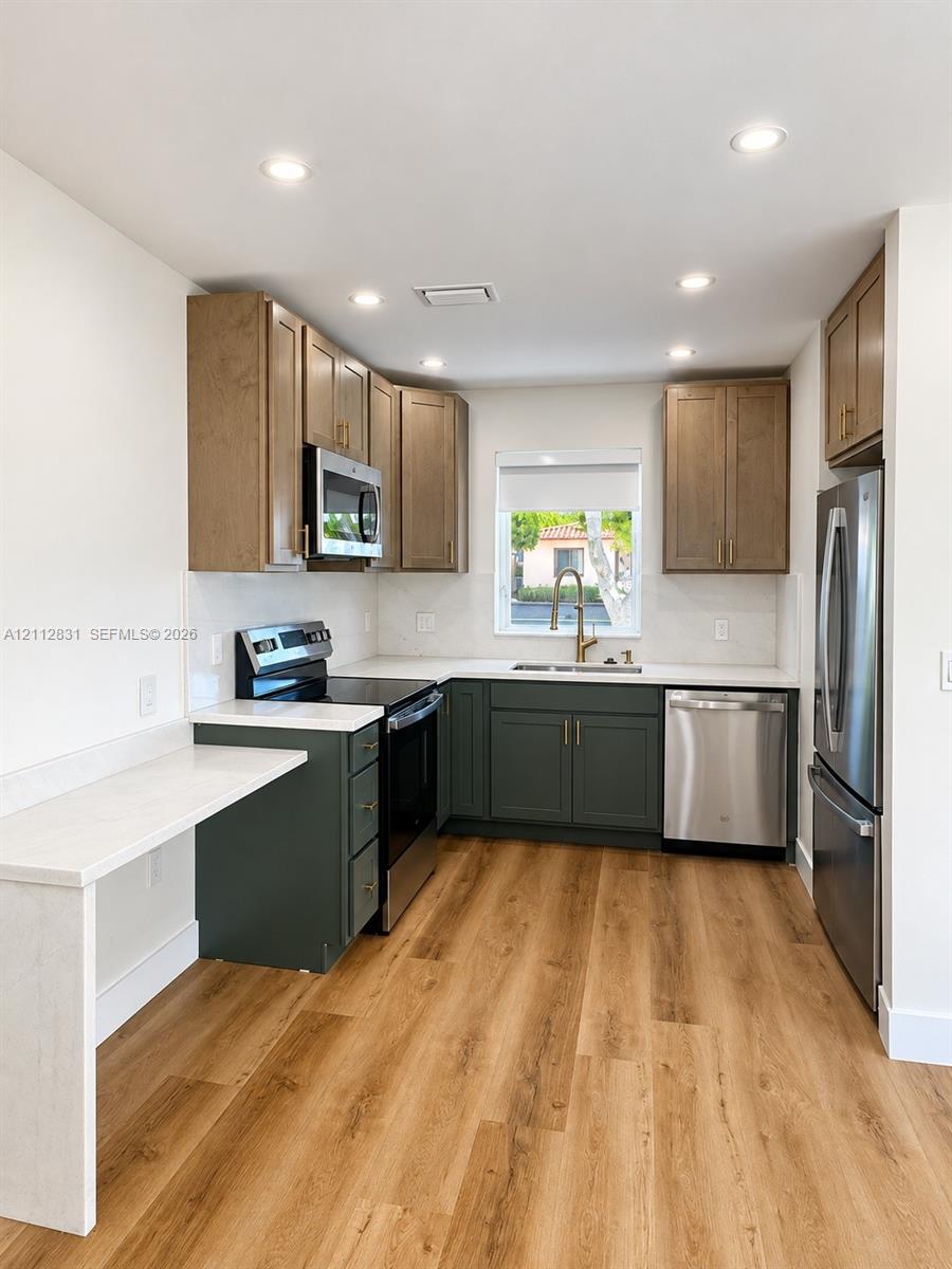 Kitchen featuring wood-finish flooring, two-tone cabinetry, stone-surface countertops, recessed lighting, and stainless steel appliances