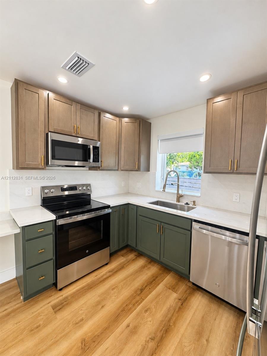 Kitchen featuring two-tone cabinetry with brass-finish hardware, stainless steel appliances, white solid-surface countertops, and wood-finish flooring
