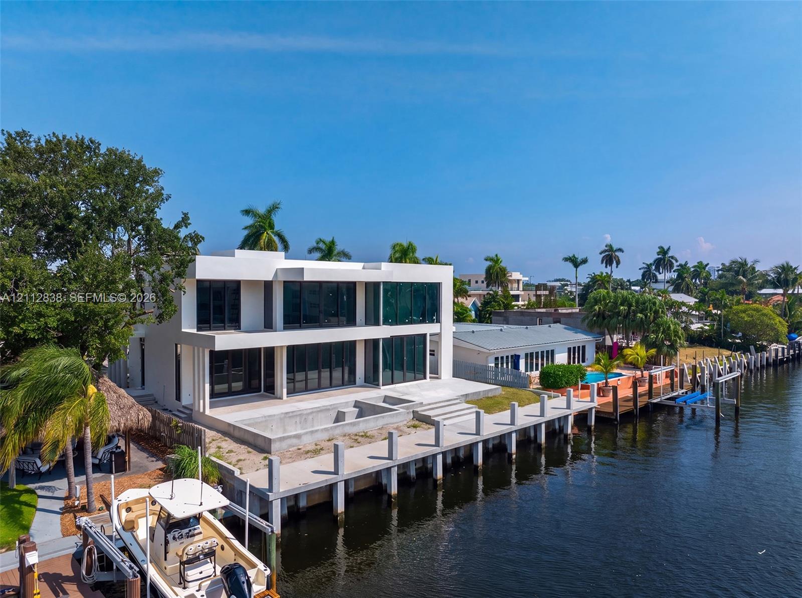 Modern two-story waterfront residence featuring an expansive rear patio, concrete dock, floor-to-ceiling glass paneling, and flat roof architecture