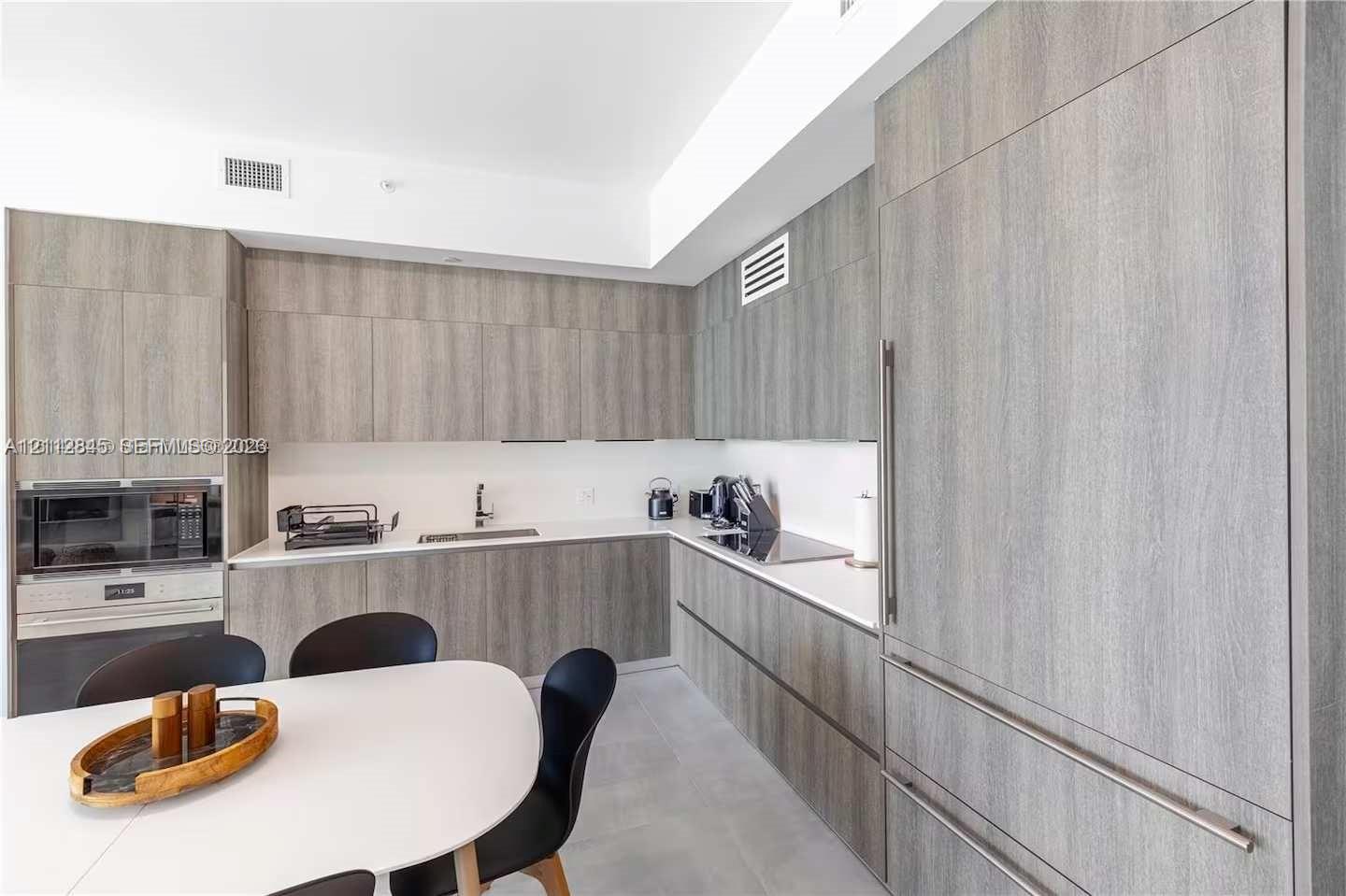 Kitchen featuring flat-panel wood-finish cabinetry, integrated panel-ready refrigerator, solid-surface countertops, built-in microwave, and flush-mount cooktop