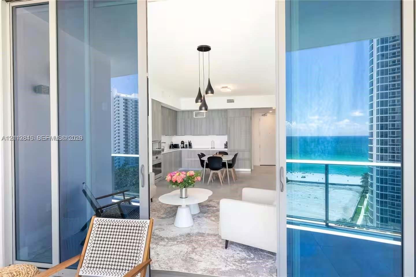 Full-height sliding glass doors opening to a covered balcony, integrated kitchen cabinetry, recessed ceiling lighting, pendant light fixture, and ocean scenery