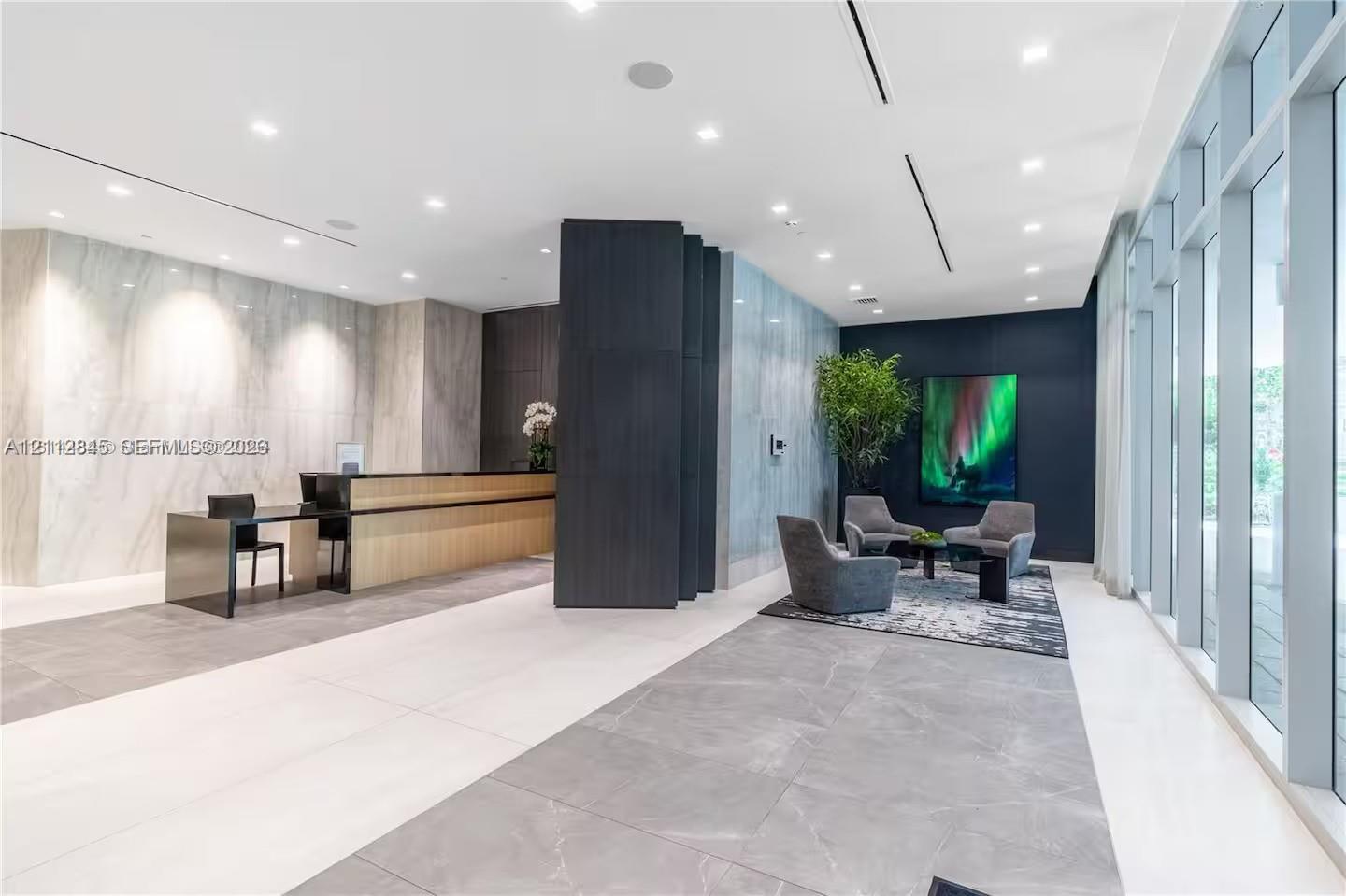 Lobby area featuring large-format tile flooring, stone-clad accent walls, floor-to-ceiling windows, recessed lighting, and a custom built-in reception desk