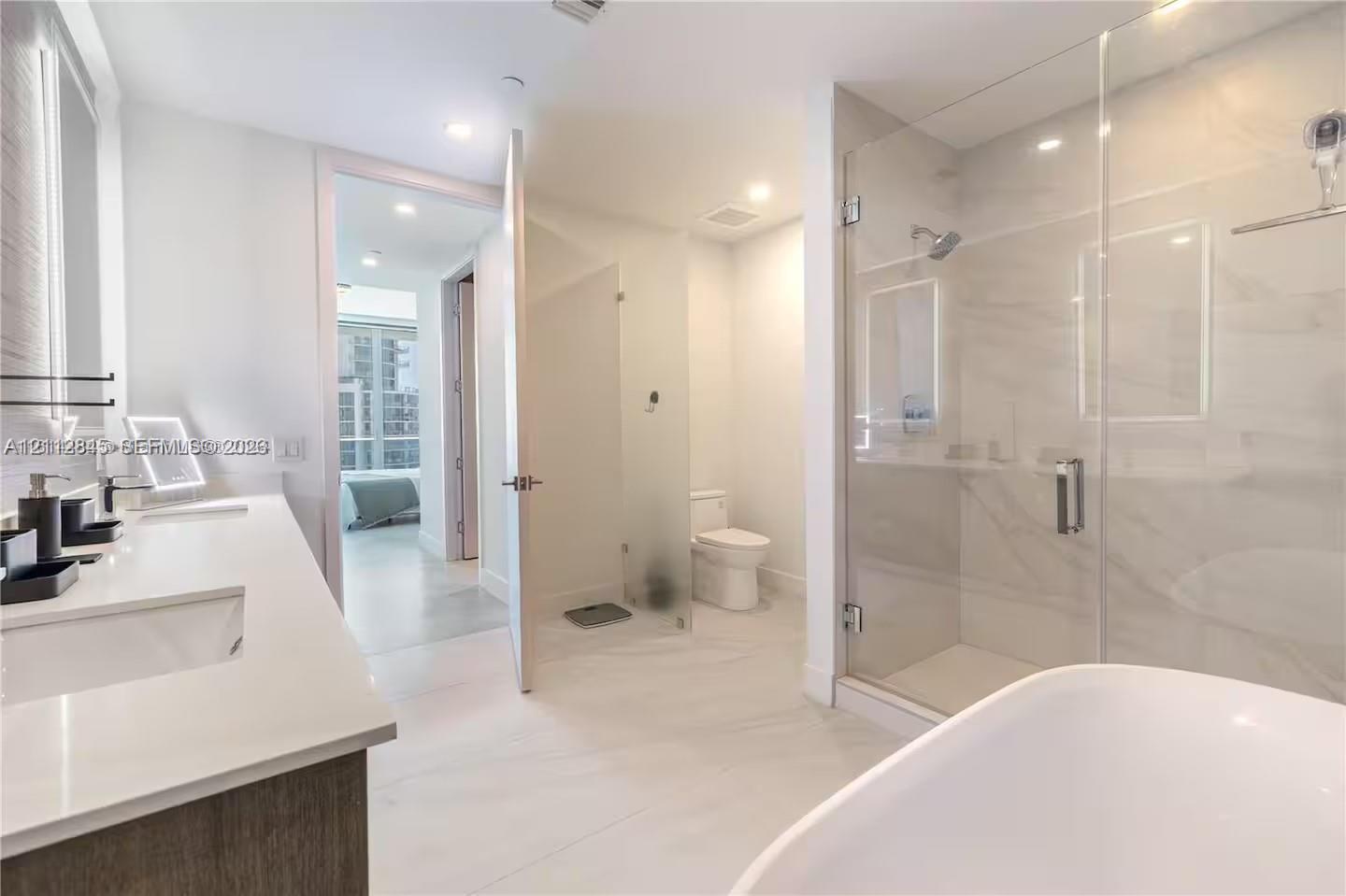 Bathroom featuring a dual-sink vanity with light-colored countertops, a freestanding soaking tub, and a glass-enclosed shower with tiled surround Bathroom featuring a dual-sink vanity with light-colored countertops, a freestanding soaking tub, and a glass-enclosed shower with tiled surround