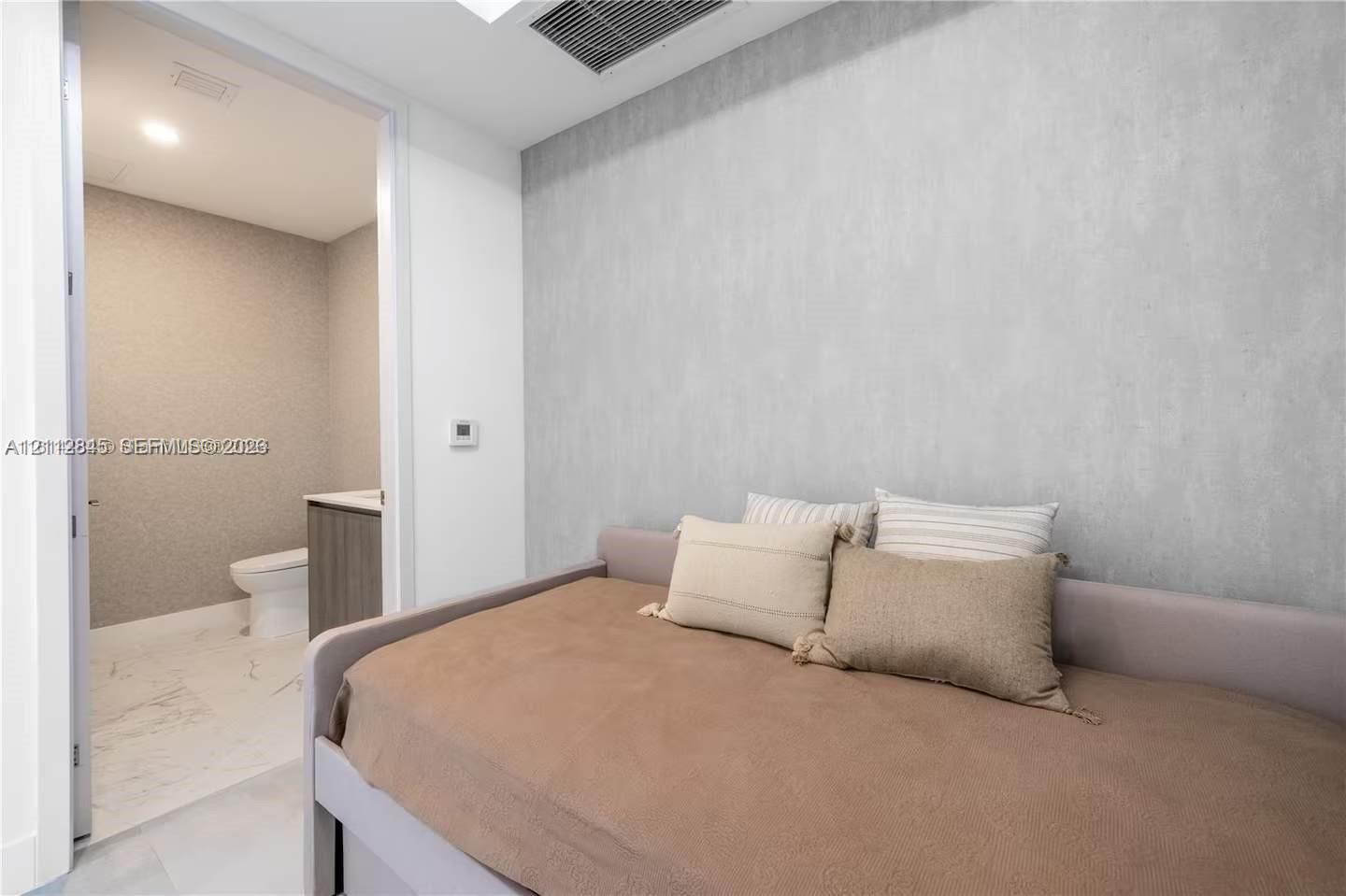 Textured accent wall, neutral interior palette, and recessed ceiling lighting, with an entry to a bathroom featuring stone-finish floor tiling and a floating vanity
