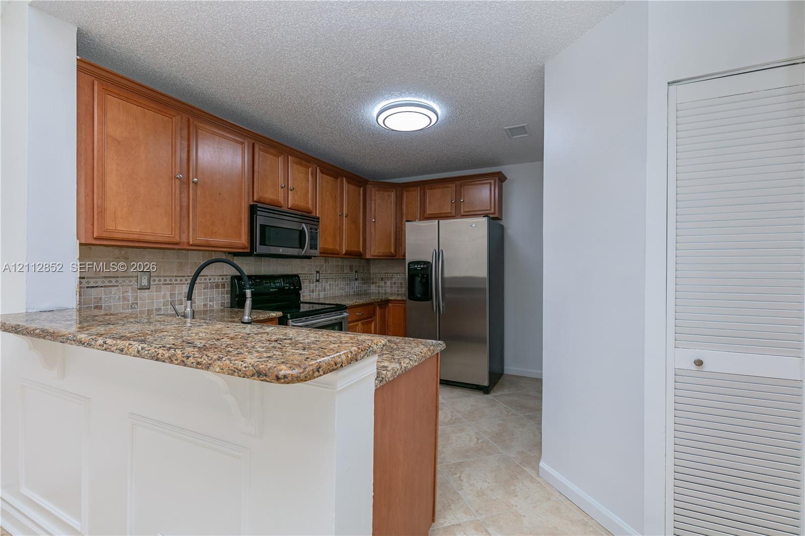 Kitchen featuring natural wood cabinetry, stone-finish countertops, stainless steel appliances, a decorative tiled backsplash, and tile flooring