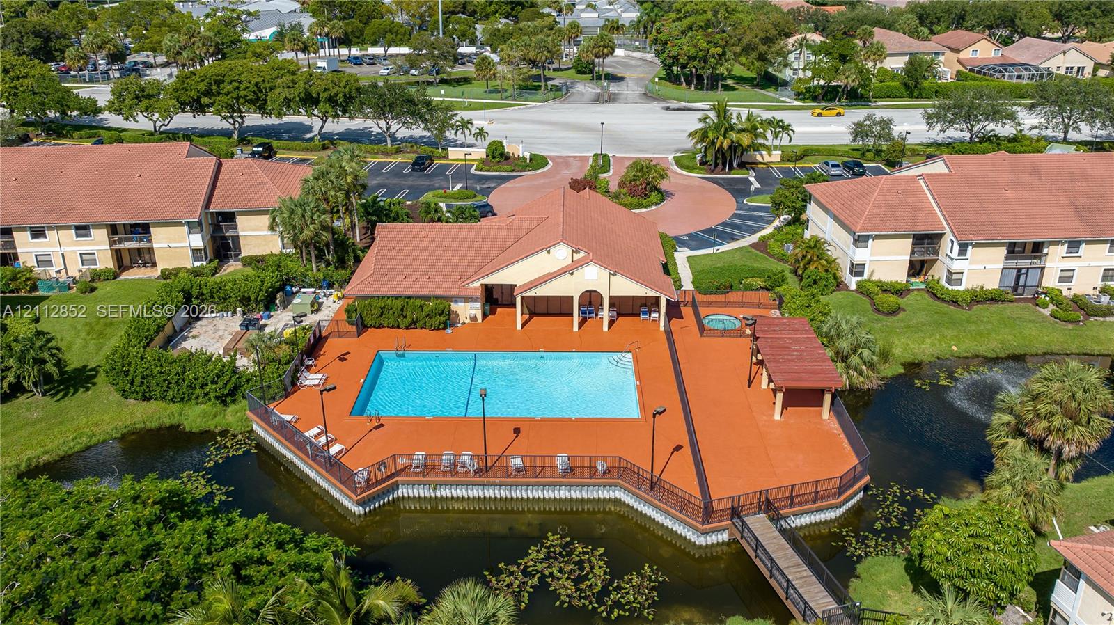 Community pool area featuring a perimeter deck, attached spa, covered pavilion, and pedestrian bridge over a water feature