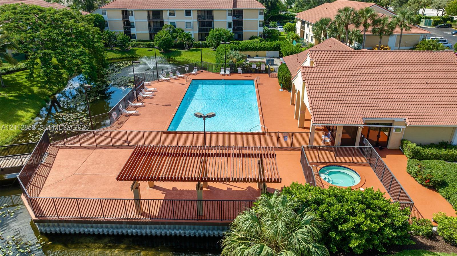 Community recreation area featuring a swimming pool, spa, water fountain, and wooden pergola set against a water feature