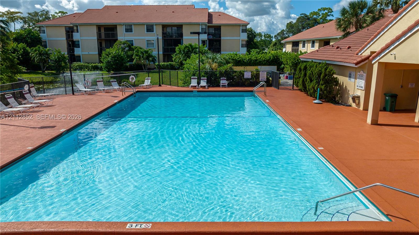 In-ground swimming pool with surrounding deck, metal perimeter fencing, and structured water feature