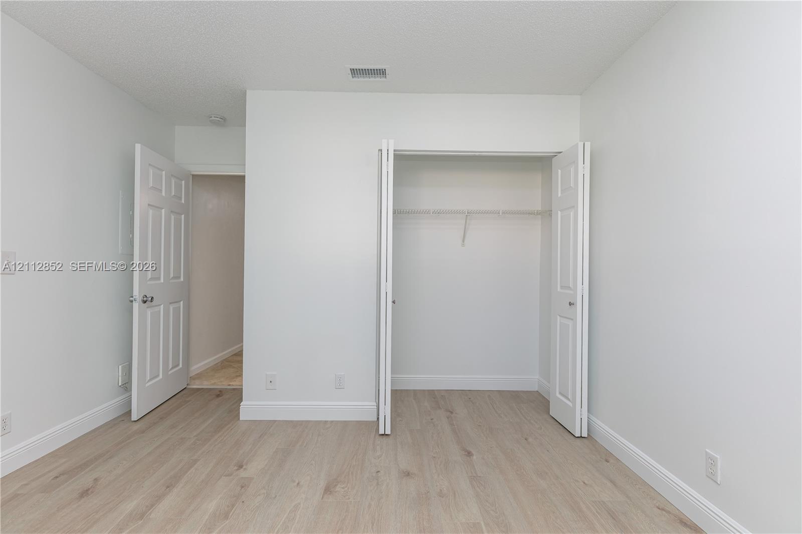 Room featuring wood-finish flooring, white walls, and a closet with bifold doors and built-in shelving