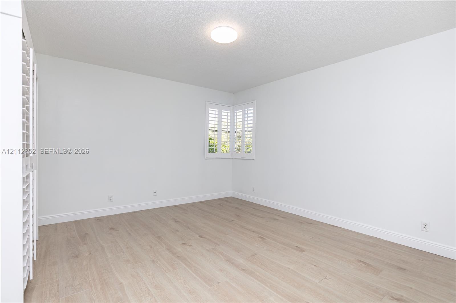 Neutral-toned room featuring wood-finish flooring, white plantation shutters, and a flush-mount ceiling light fixture
