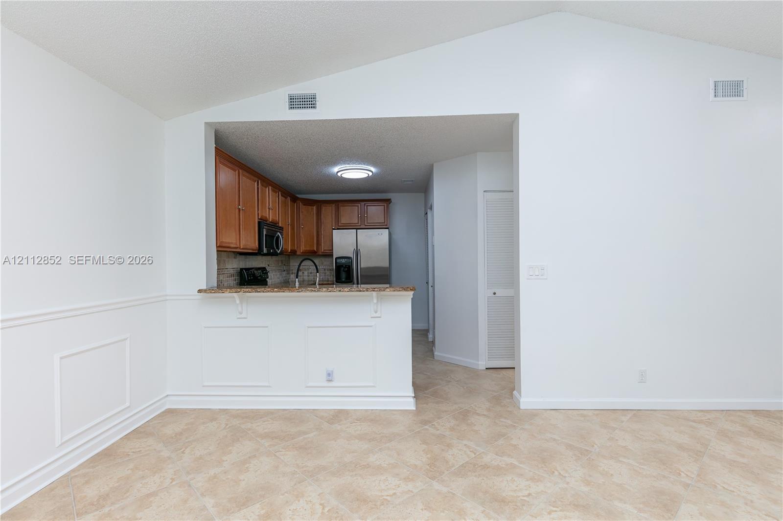 Vaulted ceiling featuring a breakfast bar with stone-finish countertop, wooden cabinetry, stone backsplash, and neutral tile flooring