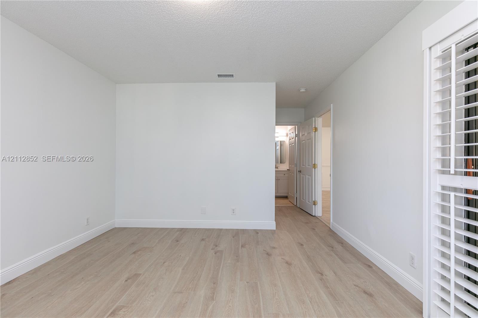 Room featuring light-toned wood-finish flooring, white walls, and interior louvered shutters