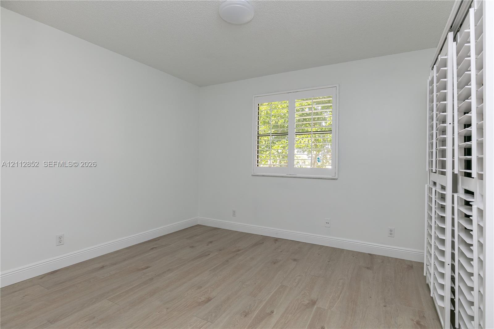 Room featuring wood-finish flooring, a window with louvered shutters, and bi-fold louvered closet doors